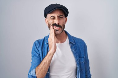 Hispanic man with beard standing over isolated background touching mouth with hand with painful expression because of toothache or dental illness on teeth. dentist 