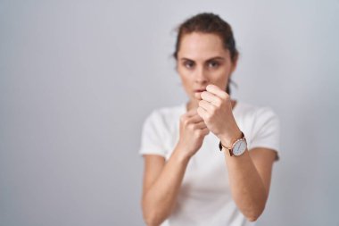 Güzel esmer kadın izole arka planda duruyor. Yumruk savunma hareketleriyle dövüşmeye hazır. Kızgın ve üzgün bir yüz, sorundan korkuyor. 