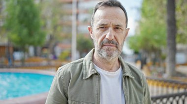 Parkta ciddi bir ifadeyle duran orta yaşlı bir adam.