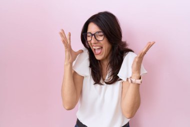 Orta yaşlı İspanyol kadın, günlük beyaz tişört ve gözlük giyip başarıyı kutlamak için deli ve deli gibi kutlama yaparken kollarını kaldırmış ve gözlerini kapatmış heyecanlı çığlıklar atıyordu. Kazanan konsept 