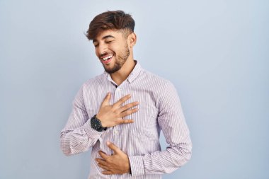 Mavi arka planda duran sakallı bir Arap adam gülümseyerek ve kahkahalarla gülüyor çünkü elleri vücutta olan komik, çılgın bir şaka.. 