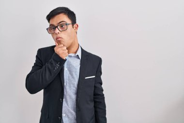Down sendromlu genç İspanyol bir adam iş stili giyiyor ve çenesi üzerinde soru soruyor. Düşünceli bir yüz ifadesi var. Düşünceli bir yüzle gülümsüyor. şüphe kavramı. 