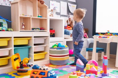 Anaokulunda rahat bir ifadeyle oynayan sevimli beyaz çocuk.