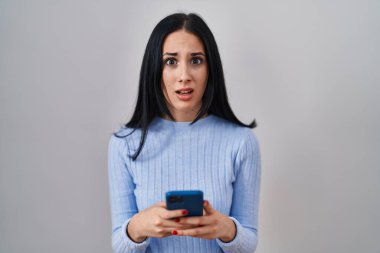 Hispanik kadın akıllı telefon kullanıyor, habersiz ve kafası karışık bir ifade. şüphe kavramı. 