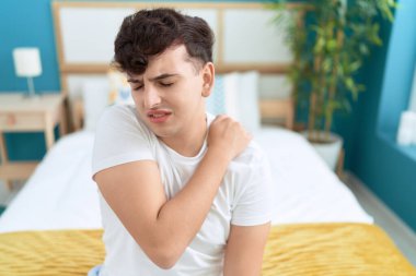 Non binary man suffering for cervical injury sitting on bed at bedroom