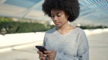 Parkta rahat bir ifadeyle akıllı telefon kullanan Afrikalı Amerikalı kadın.