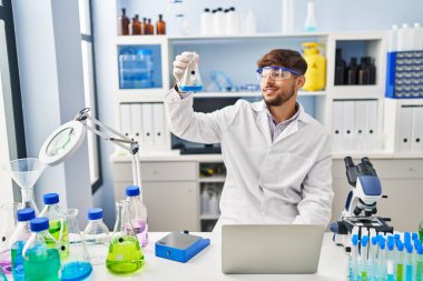 Young arab man scientist using laptop measuring liquid at laboratory
