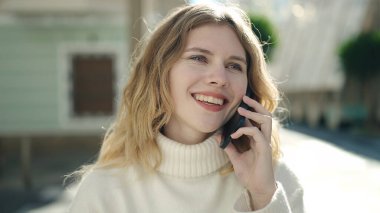 Genç sarışın kadın gülümsüyor. Kendine güveni tam. Akıllı telefondan konuşuyor.