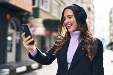 Genç İspanyol kadın sokakta müzik dinlerken kendinden emin gülümsüyor.