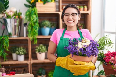 Çiçekçi dükkanında çalışan İspanyol genç bir kadın elinde çiçekle kameraya bakıyor. Seksi bir ifadeyle, neşeli ve mutlu bir yüzle.. 