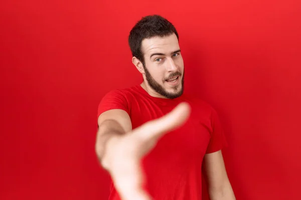 カジュアルな赤いTシャツを着た若いヒスパニック系の男性が挨拶や歓迎として握手を提供笑顔 成功したビジネス — ストック写真