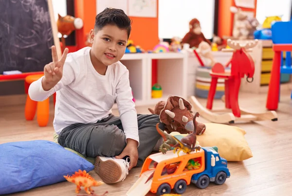 愛らしいHispanic男の子遊びとともに車と恐竜おもちゃ行います勝利ジェスチャーで幼稚園 — ストック写真