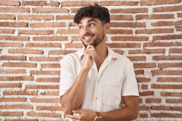 あごの質問について考える上で手でレンガの壁の背景に立ってひげを生やしたアラブ人男性は 集中的な表現 笑顔で思いやりのある顔 疑わしい概念 — ストック写真