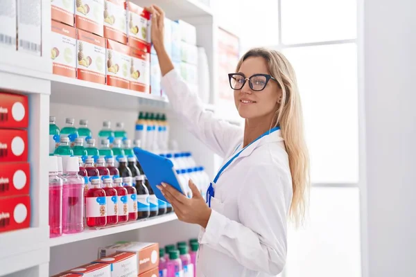 薬局で棚に製品を保持タッチパッドを使用して若いブロンドの女性薬剤師 — ストック写真