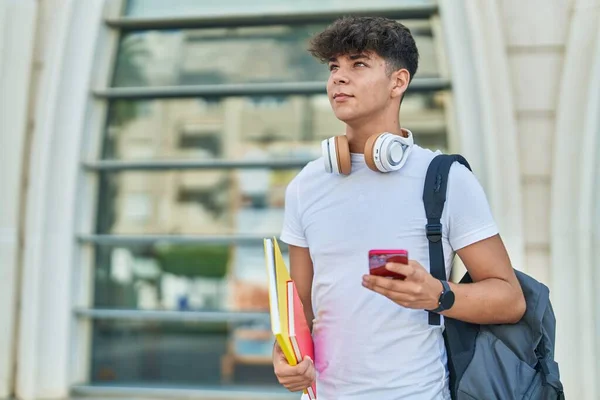 若いヒスパニック系の10代の学生が大学でスマートフォンを保持本を使用して — ストック写真