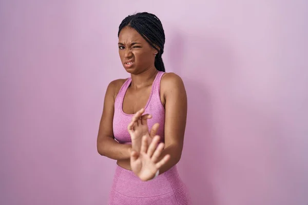 African american woman with braids wearing sportswear over pink background disgusted expression, displeased and fearful doing disgust face because aversion reaction.