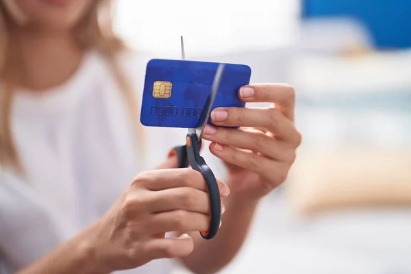 Young blonde woman cutting credit card at home