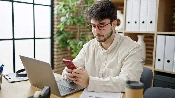 オフィスでノートパソコンやスマートフォンを使っている若いヒスパニック系の男性のビジネスワーカー — ストック写真