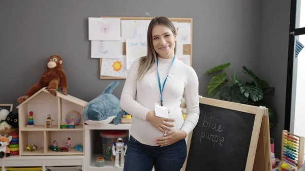 Junge Schwangere Kindergärtnerin Lächelt Selbstbewusst Und Berührt Bauch Kindergarten — Stockfoto