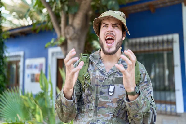 カモフラージュ軍を身に着けている若いヒスパニック系の男は 攻撃的な表現と腕を上げて狂った叫びと叫び屋外の制服 フラストレーションコンセプト — ストック写真