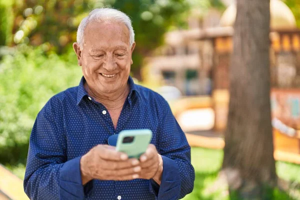 Senior Γκρίζα Μαλλιά Άνθρωπος Χαμογελά Αυτοπεποίθηση Χρησιμοποιώντας Smartphone Στο Πάρκο — Φωτογραφία Αρχείου
