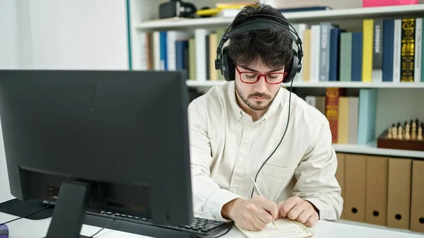 Young Hispanic Man Student Using Computer Headphones Writing Notes Library — Stock Photo, Image