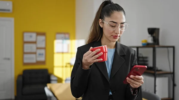 年轻漂亮的惊慌失措的女商人在办公室用智能手机喝咖啡 — 图库照片