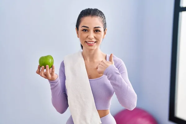 スポーツウェアとタオルを身に着けている若い女性食べる緑のリンゴ指差し指に一人の自己笑顔幸せと誇り — ストック写真