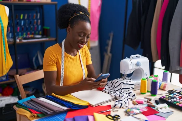 非洲裔美国妇女裁缝笑着自信地使用智能手机在缝纫工作室 — 图库照片