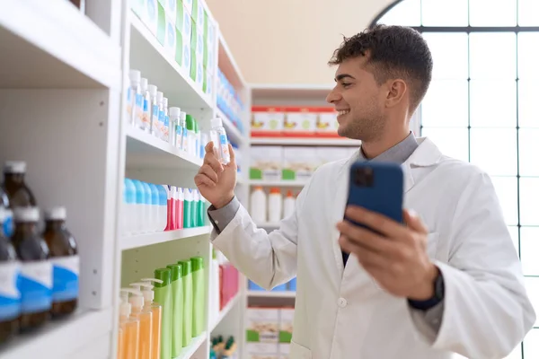 Young Hispanic Man Pharmacist Using Smartphone Holding Medication Bottle Pharmacy — Stock Photo, Image