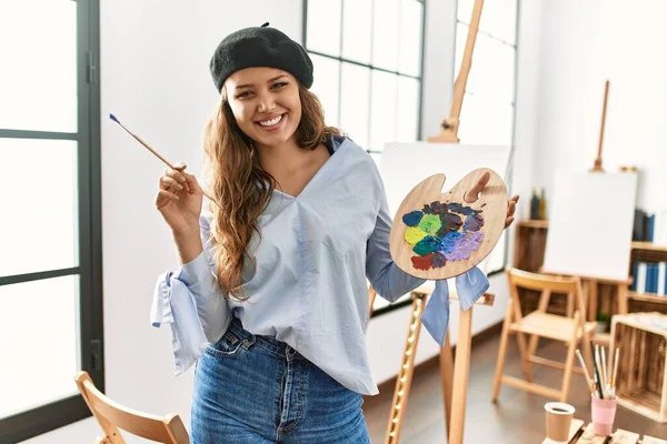 若い美しいヒスパニック女性アーティスト笑顔自信を持って保持絵筆とパレットでアートスタジオ — ストック写真