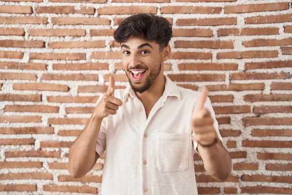 ひげをレンガの壁の背景の上に立っているアラブ人の男が幸せと面白い顔を持つカメラに指を指している 良いエネルギーと振動は — ストック写真