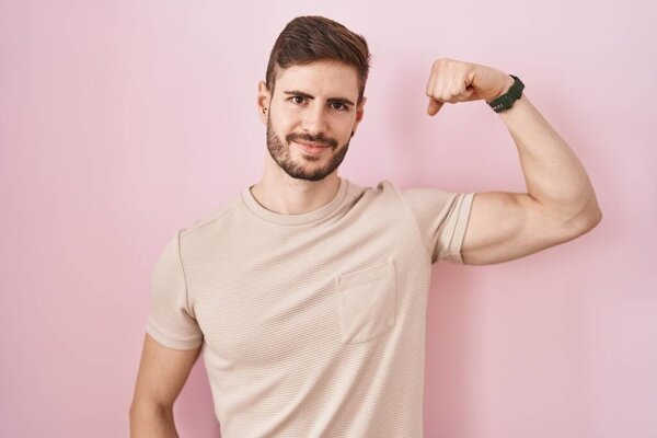 Hispanic man with beard standing over pink background strong person showing arm muscle, confident and proud of power 