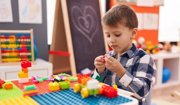 幼稚園のテーブルの上に座っている建設ブロックで遊んで愛らしい白人少年 — ストック写真