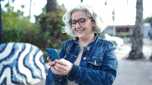 stock image Middle age woman with grey hair using smartphone at park