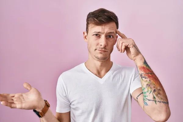 ピンクの背景の上に立つ白人男性は混乱し コピースペースを示し 額に指を指す開いてヤシに悩まされました 考えてみてください — ストック写真