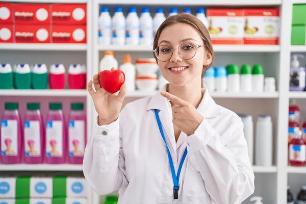 Молодая Белая Женщина Работающая Аптеке Держит Красное Сердце Улыбаясь Показывая — стоковое фото