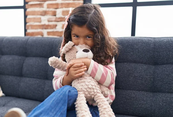 Adorável Menina Hispânica Beijando Abraçando Ursinho Sentado Sofá Casa — Fotografia de Stock