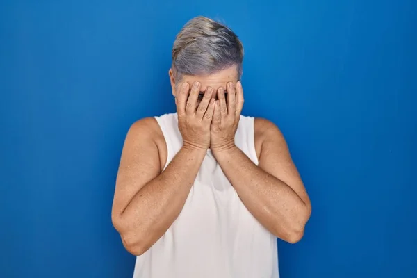 泣きながら手で顔を覆う悲しい表情で青い背景の上に立つ中年の白人女性 うつ病の概念 — ストック写真