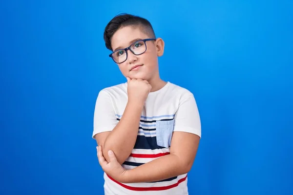 若いヒスパニック系の子供の質問については 集中的な表現を考えて顎の手で青の背景に立っている 思慮深い顔で笑顔 疑わしい概念 — ストック写真