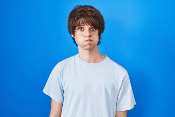 Hispanic Young Man Standing Blue Background Puffing Cheeks Funny Face — Foto Stock