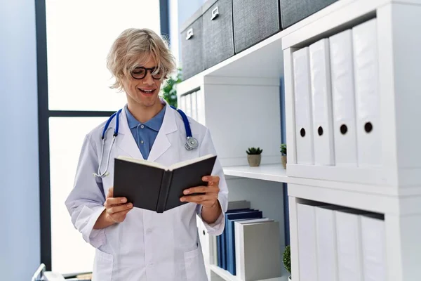 Young Blond Man Doctor Smiling Confident Reading Book Clinic — Stockfoto