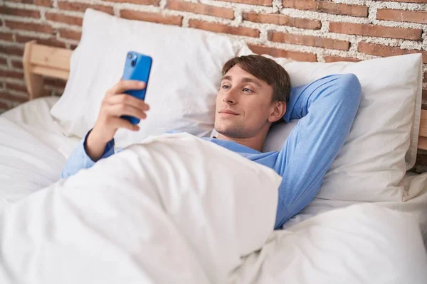 Młody Biały Mężczyzna Pomocą Smartfona Leżącego Łóżku Sypialni — Zdjęcie stockowe