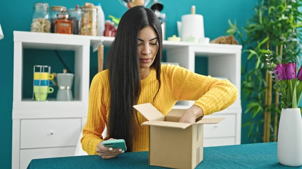 Young Beautiful Hispanic Woman Unpacking Package Holding Smartphone Dinning Room — Stock Photo, Image