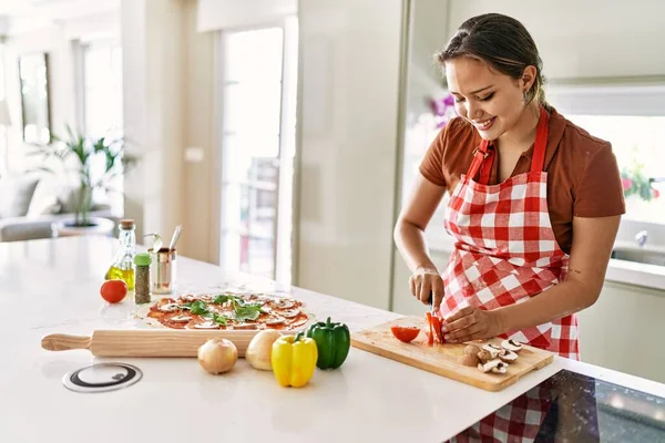 年轻美丽的惊慌失措的女人微笑着在厨房切西红柿 — 图库照片