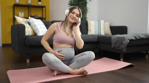 坐在瑜伽垫上听音乐的年轻孕妇 — 图库照片