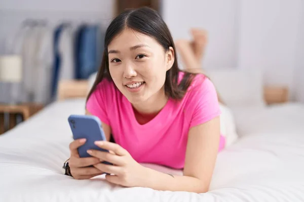 中国女人用智能手机躺在床上 — 图库照片