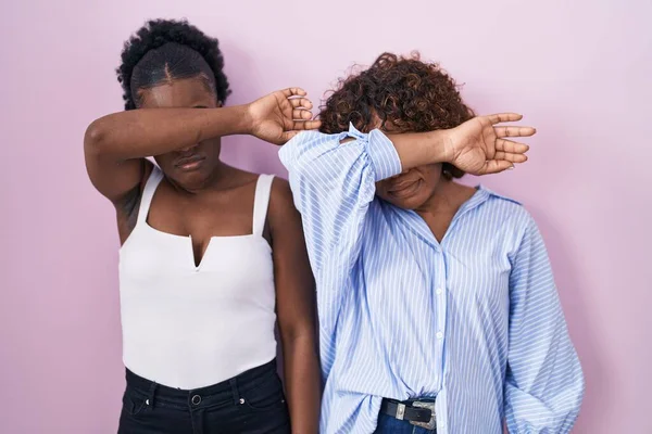 ピンクの背景に立っている2人のアフリカ人女性が腕で目を覆い 真剣に悲しい顔をしている 目立たず隠し拒否の概念 — ストック写真