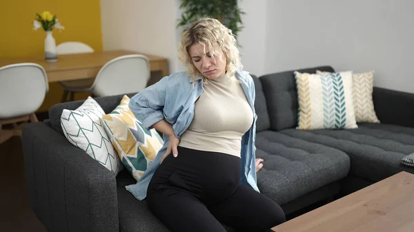 年轻的孕妇坐在家里的沙发上背痛 — 图库照片