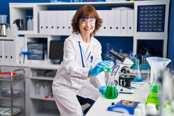 中年妇女科学家在实验室将液体倒在试管上 — 图库照片